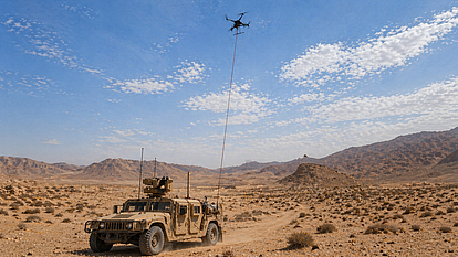 Tethered drone operations for military monitoring Tethered drone above a military vehicle in desert terrain during airborne monitoring operations.